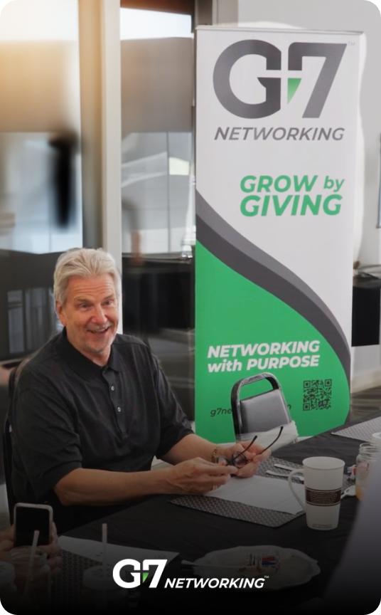 A man sitting in front of a G7 banner that says "Grow By Giving"